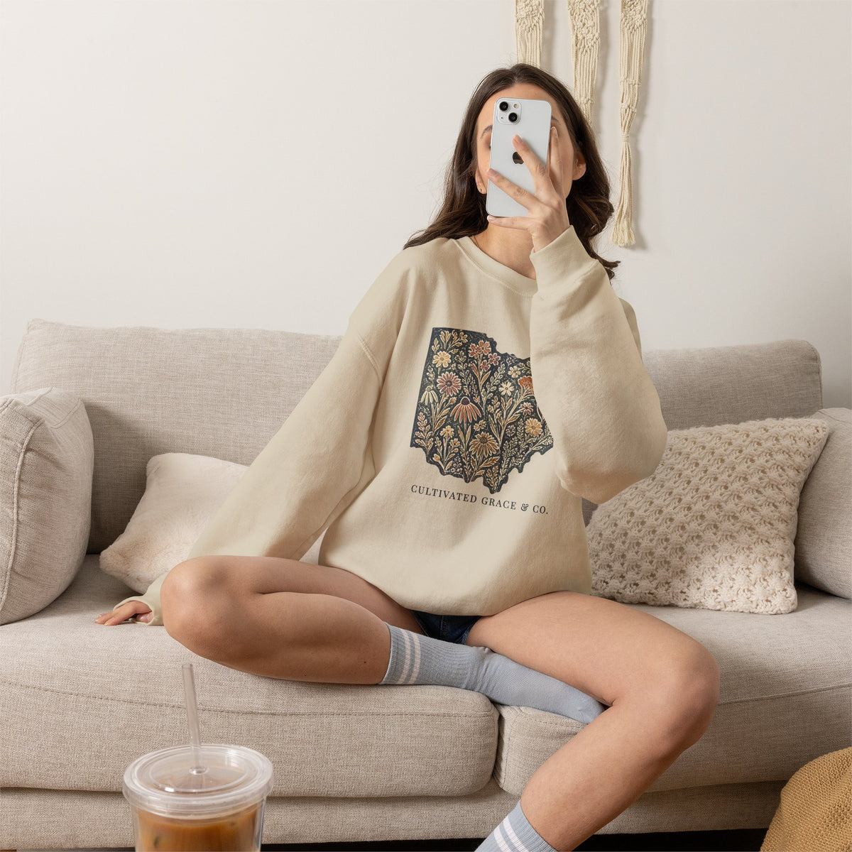 Floral Ohio crewneck in Sand worn seated on a sofa