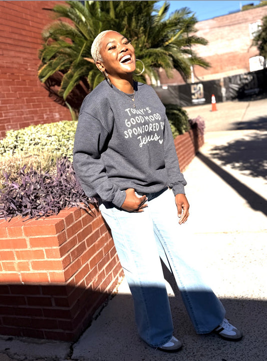 Dinee laughing outdoors in the heather gray Today's Good Mood Sponsored by Jesus sweatshirt with light wide-leg jeans