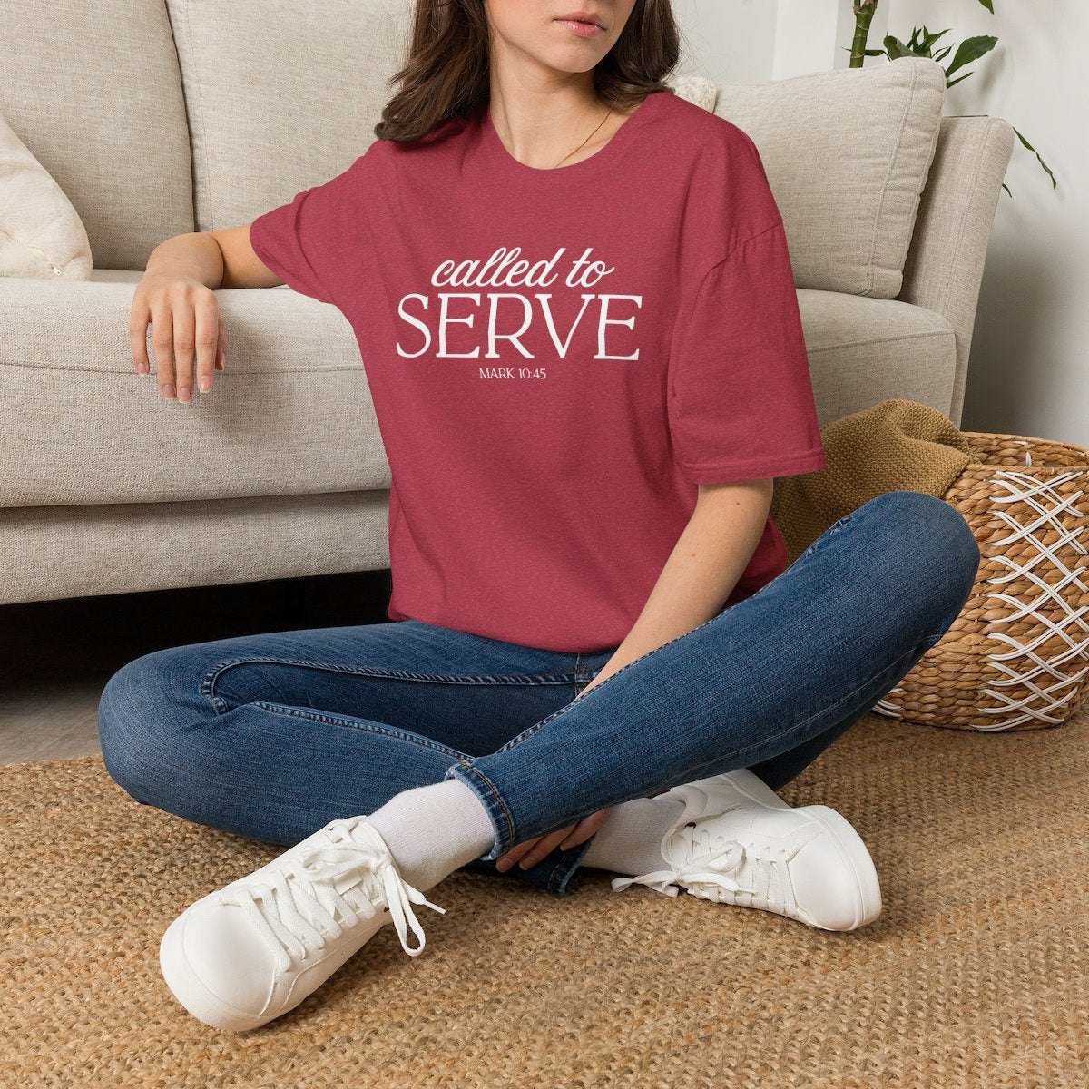 Woman seated wearing the Called to Serve tee in Heather Cardinal with jeans and white sneakers