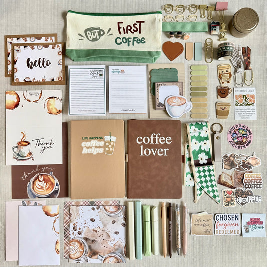 Coffee Lover Box contents arranged flat: Coffee Lover and Coffee Helps journals, two notepads, coffee pouch, pens, highlighters, cards, bookmarks and assorted accessories. Colors and individual items vary.