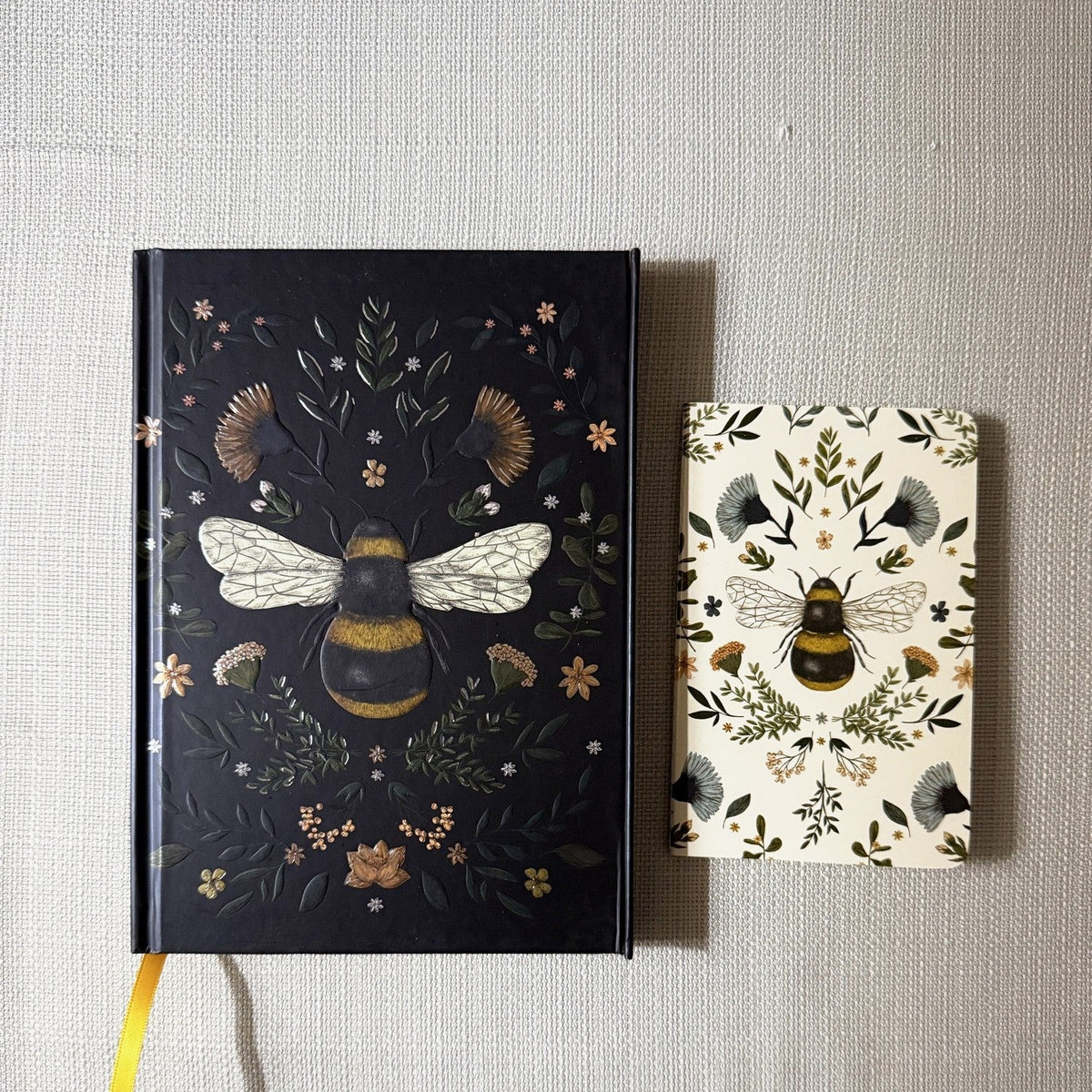 Black botanical bee journal and cream mini bee notebook from the Honey Bee Box; colors vary.