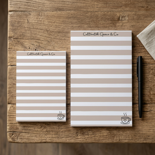 Coffee Stripes notepads in both sizes with a pen on a rustic wood table