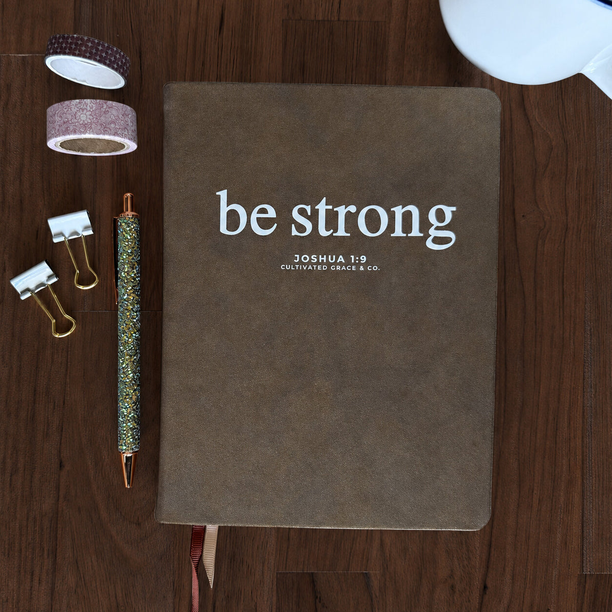 Cultivating Faith Deluxe Journal, Be Strong in Shimmer Brown, on an espresso-brown tabletop; styling props not included