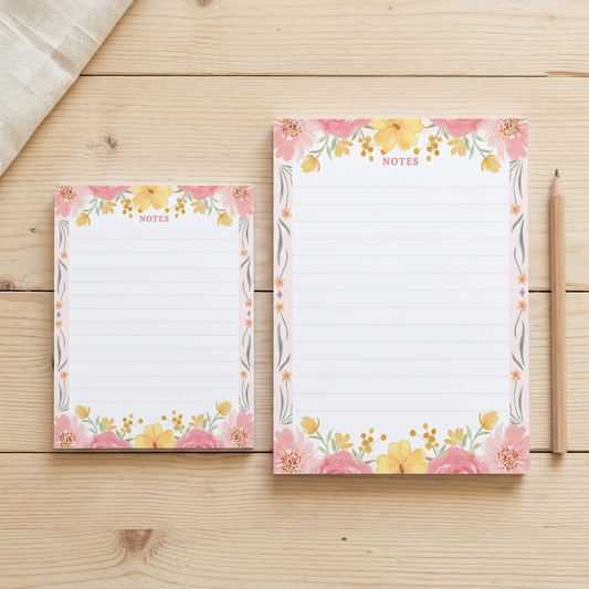 Pink and yellow floral border notepads in both sizes on a rustic wood table